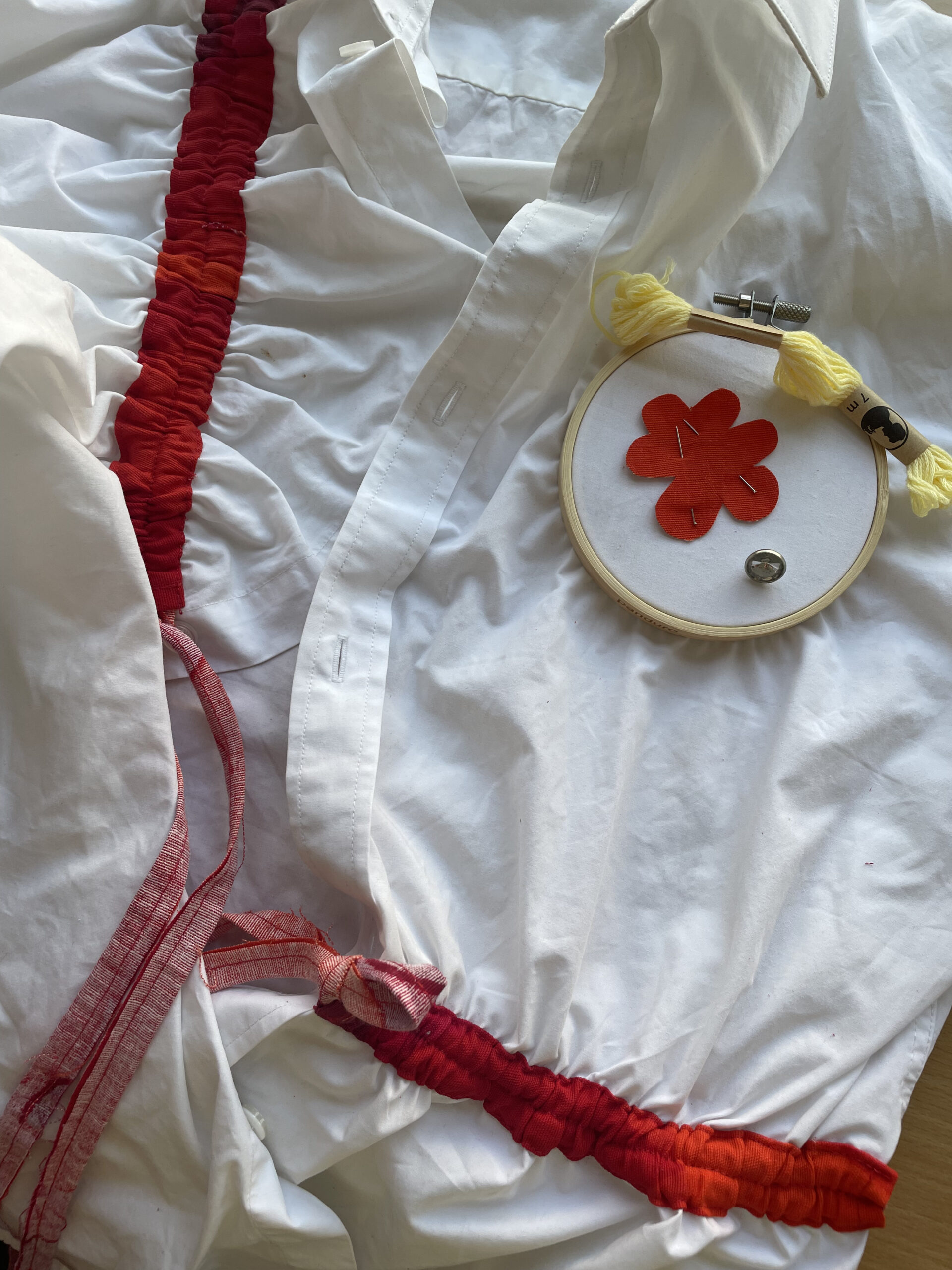 Upcycled white shirt featuring red accents and an actively used embroidery hoop